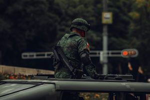 A soldier in camouflage uniform stands on a military vehicle in Mexico City, CDMX.